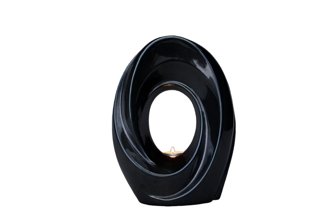 Glossy black The Passage Ceramic Urn with a hollow circular center and a lit candle visible through the opening.