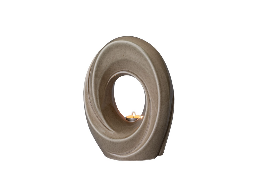 The Passage taupe ceramic urn with a swirling oval form and a built in candle holder with a lit candle.