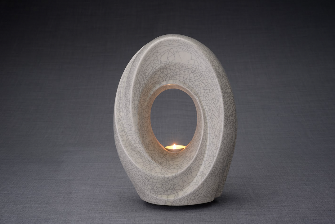 Crackled beige The Passage ceramic urn with a circular hollow center and a lit candle inside.