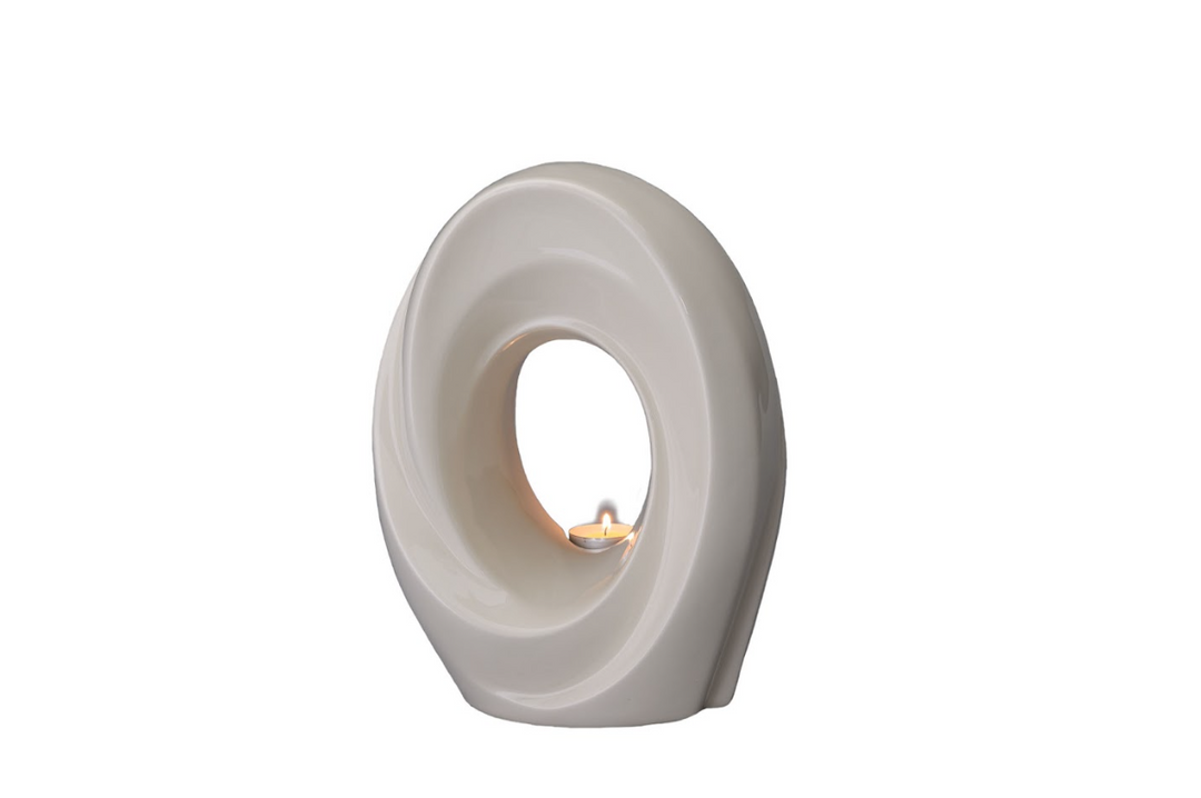 Cream ceramic The Passage Urn featuring a soft spiral design and a candle lit in the central opening.