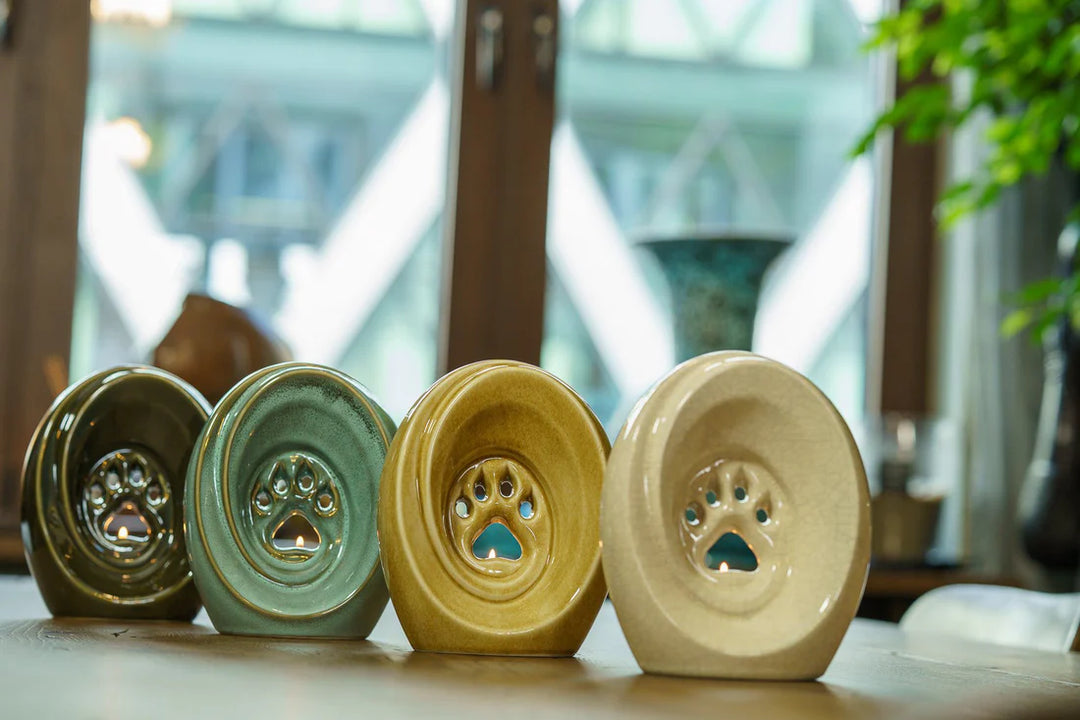 Row of paw print ceramic urns with built in candle holders in green and beige glazes.