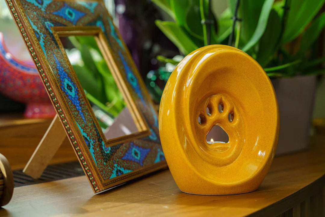 Yellow paw shaped ceramic urn with built in candle holder on a wooden surface