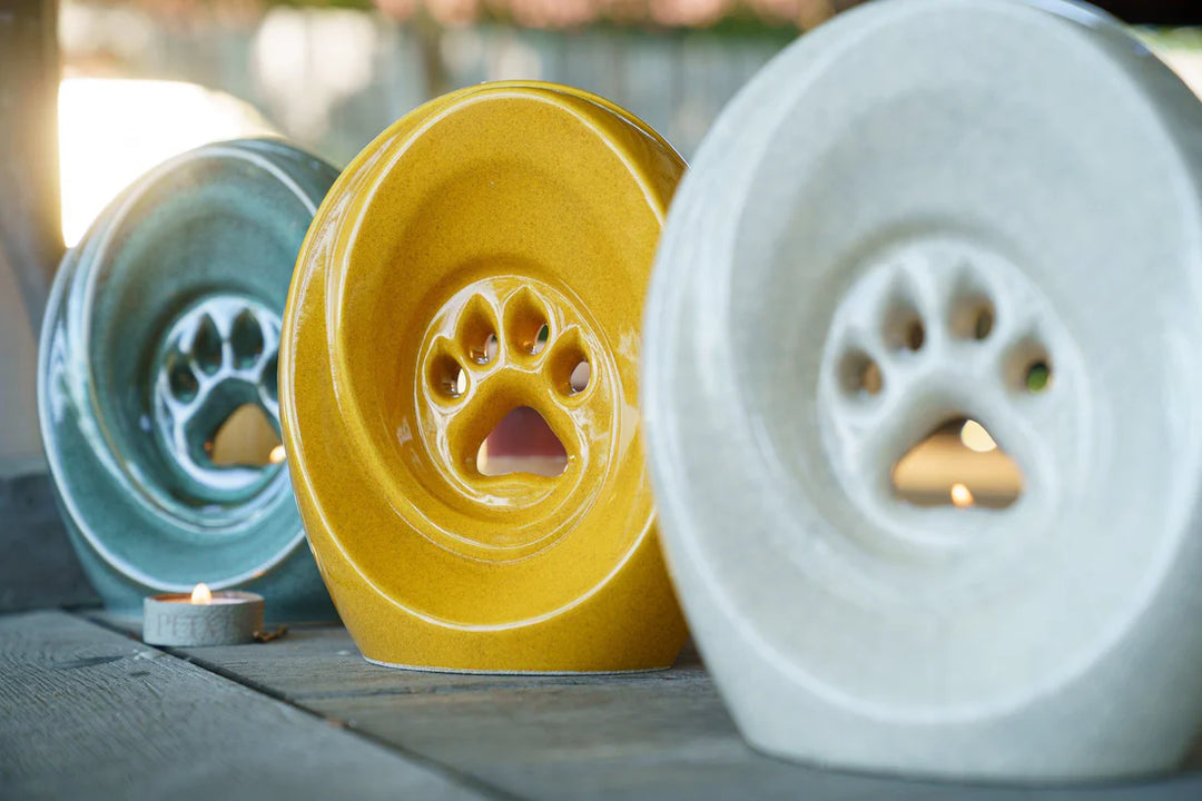 Row of colorful ceramic paw print urns in turquoise yellow and gray with built in candle holders and paw pad openings