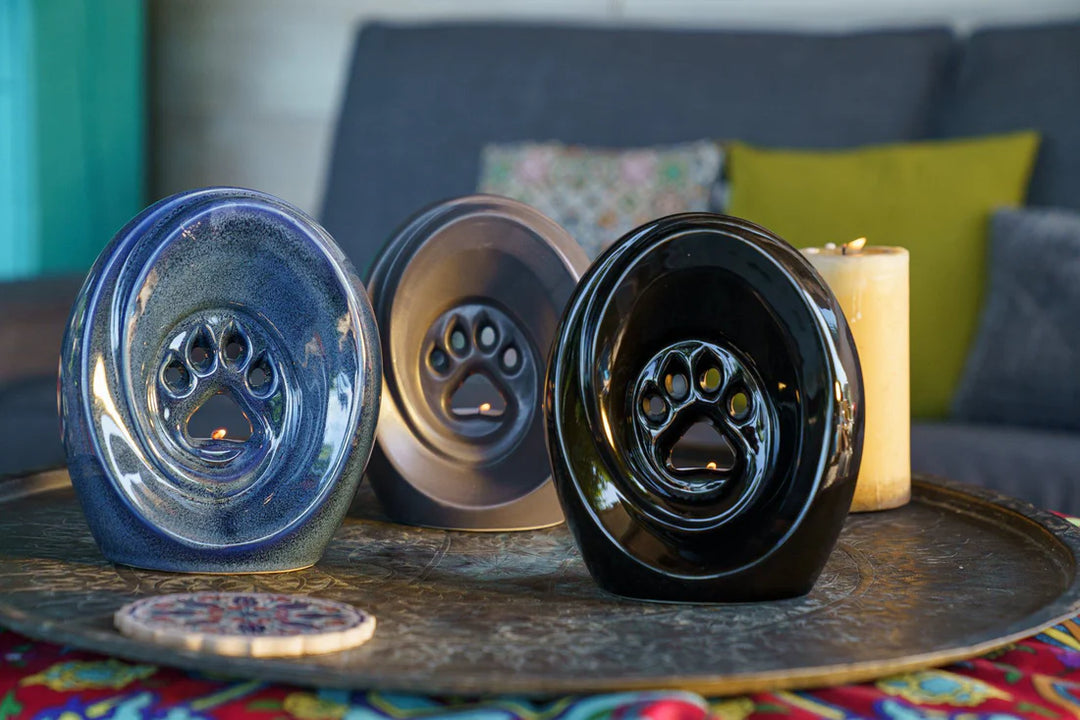 Blue, gray, and black paw print ceramic urns with built-in candle holders displayed on a tray.