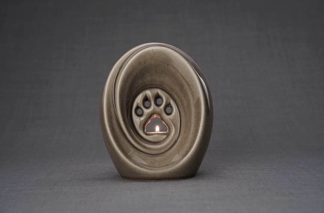 Taupe ceramic paw print urn with built in candle holder on a neutral gray background