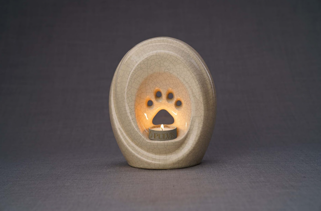 Cream crackle glaze paw print pet urn with built in candle holder and lit candle against a gray backdrop