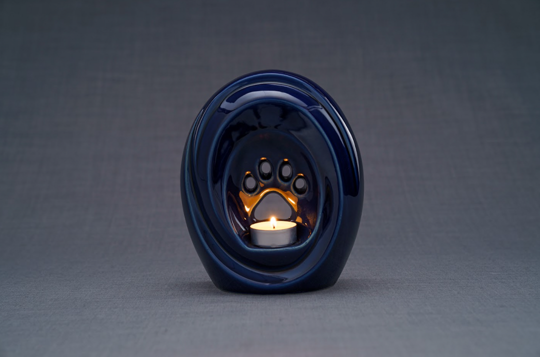 Dark blue ceramic urn with built in candle holder and a lit candle visible