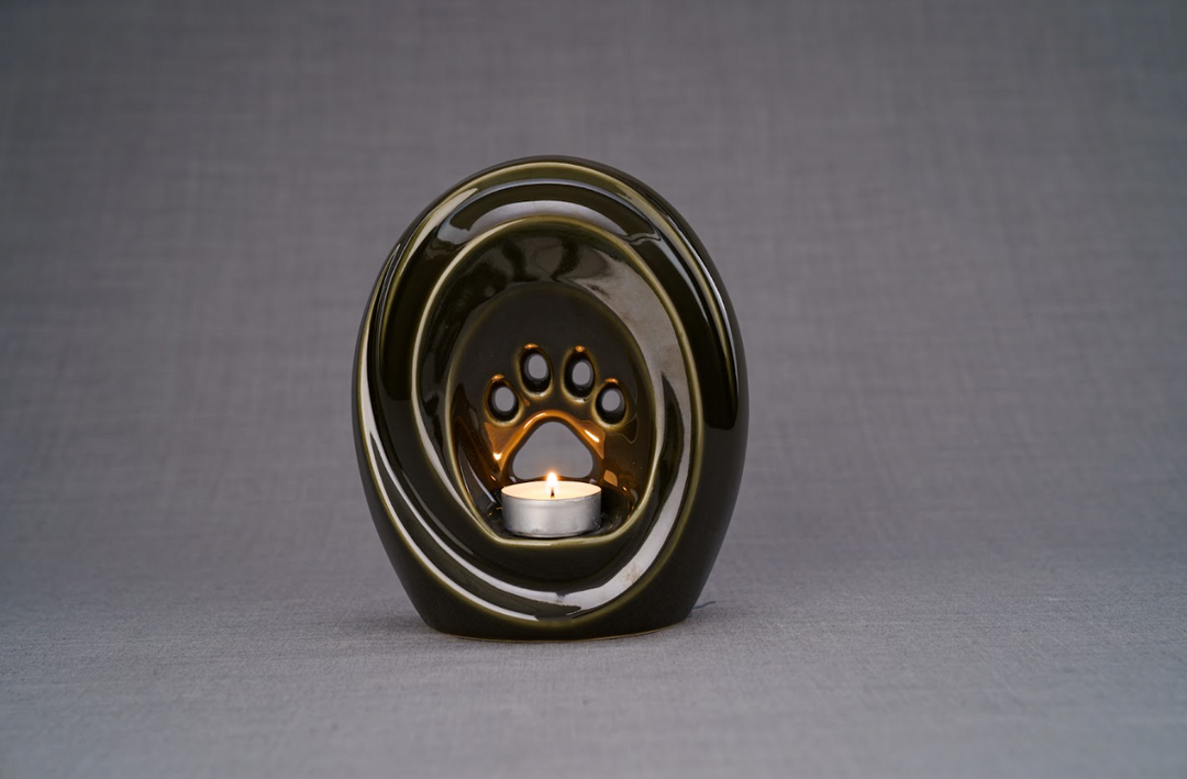 Dark glossy Paw Ceramic Urn with a candle holder in the paw recess, displayed on a textured surface