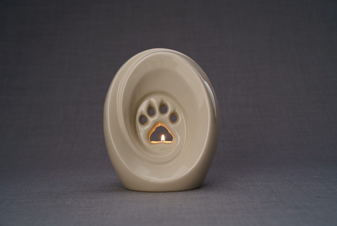 Beige Paw Ceramic Urn with built in candle holder and a small flame against a neutral gray backdrop