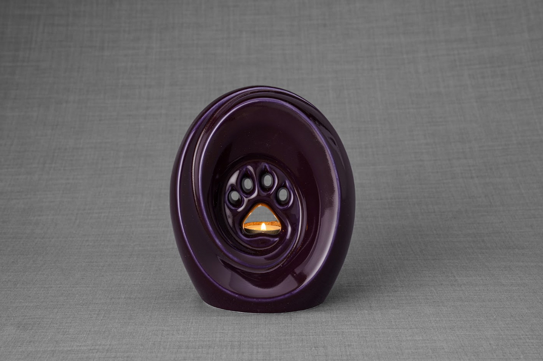 Dark purple paw print ceramic urn with built-in candle holder, a memorial for a beloved pet.
