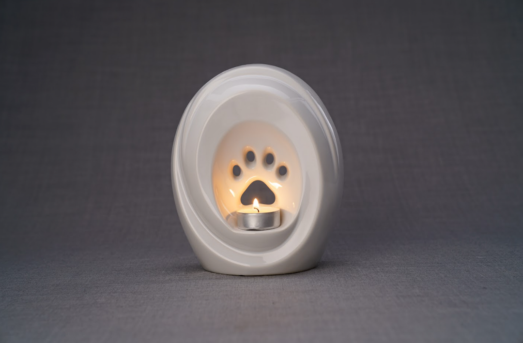 White paw print ceramic urn with built in candle holder and a metal tealight cup lit inside.