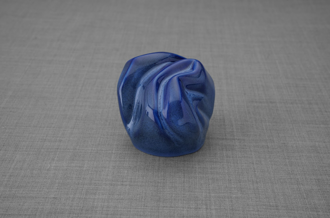 Blue ceramic keepsake urn with swirling folds on a gray surface