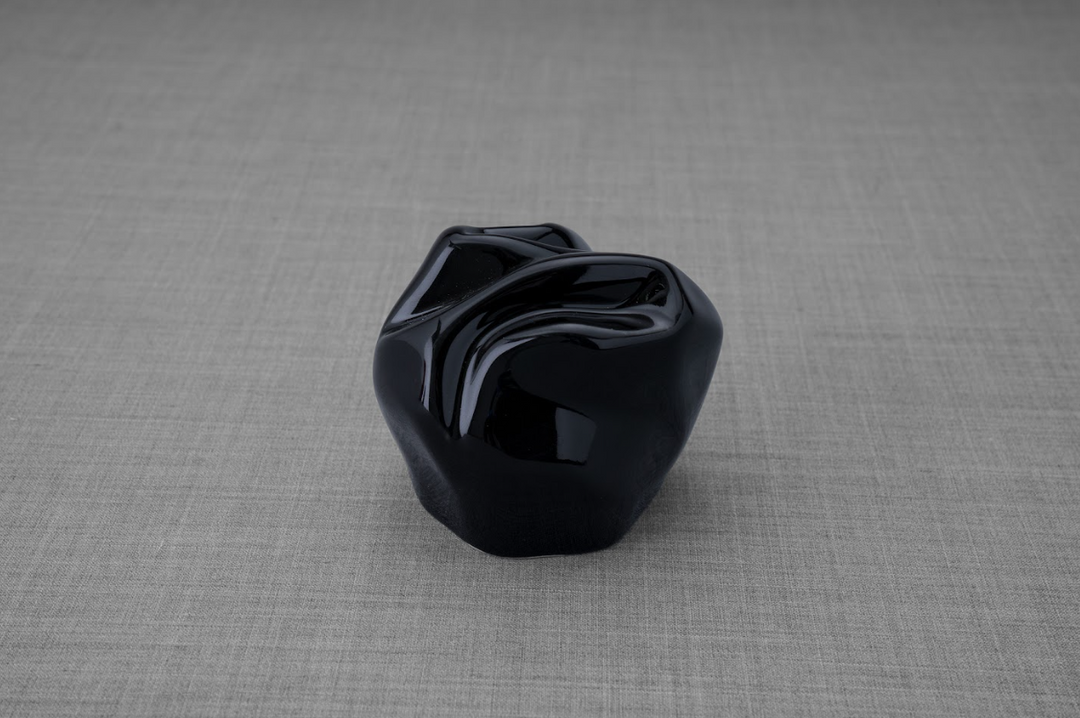 Precious ceramic keepsake urn in glossy black with rounded folds on a gray backdrop