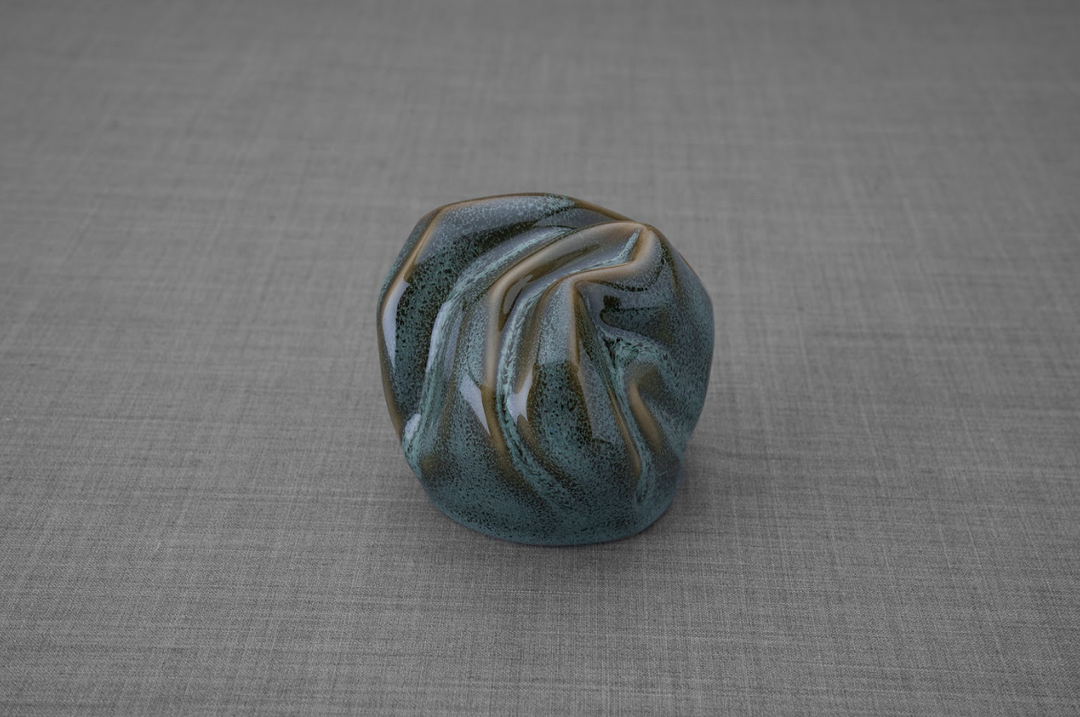 Precious ceramic keepsake urn with teal glaze and cream swirls on a gray fabric backdrop