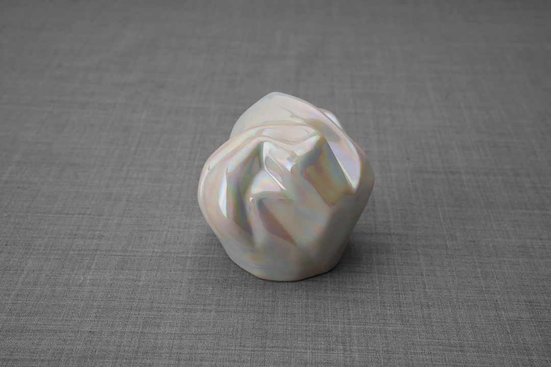 Iridescent pearl ceramic keepsake urn with rounded folded form on gray fabric background