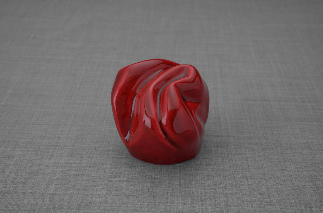 Red glossy ceramic keepsake urn with folded drapery texture on a gray background