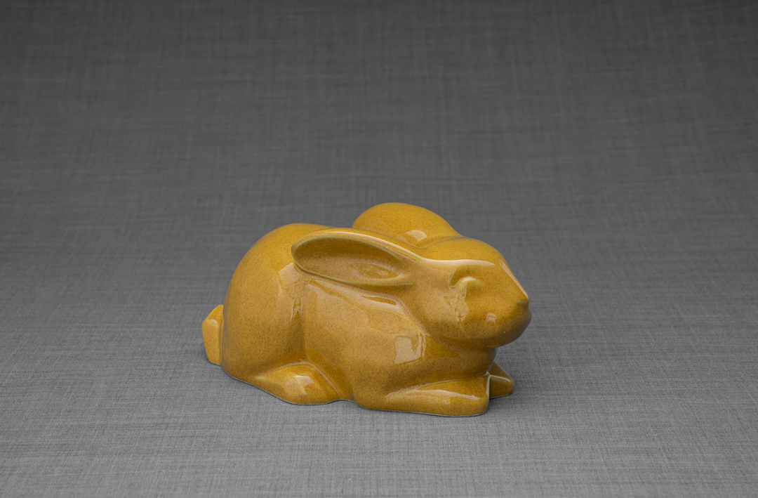 Amber gold glazed ceramic rabbit urn in a reclining pose, a heartfelt memorial for a beloved bunny.