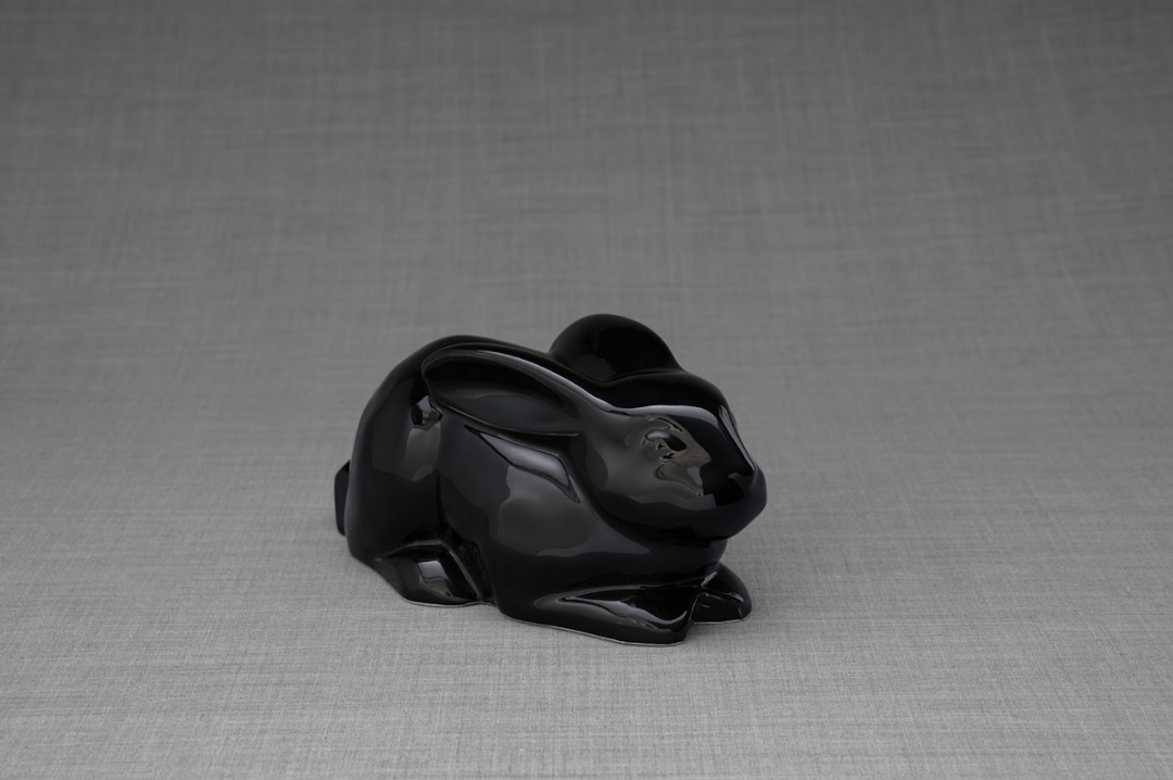 Glossy black ceramic rabbit urn on a gray backdrop