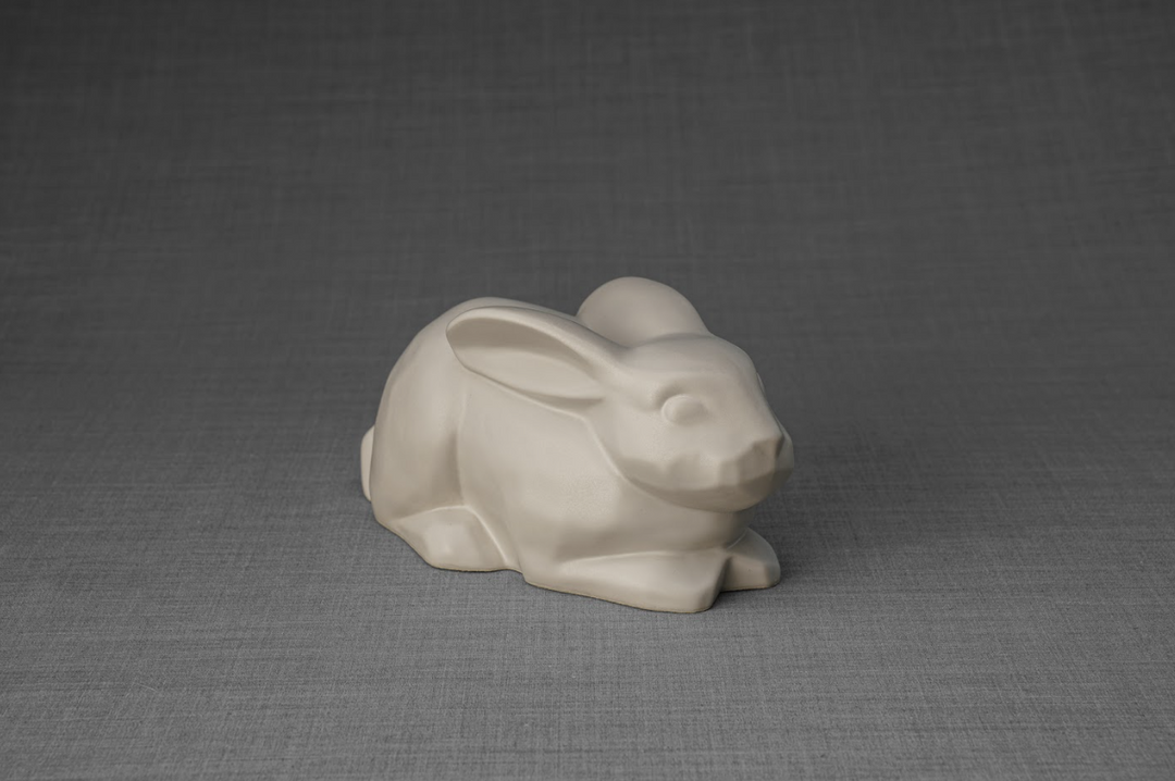 Ivory ceramic rabbit urn resting on a neutral gray surface