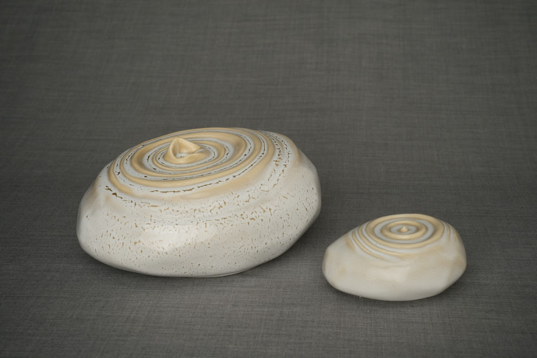 Two beige speckled ceramic resonance urns in different sizes with tan spiral rings on top surfaces.