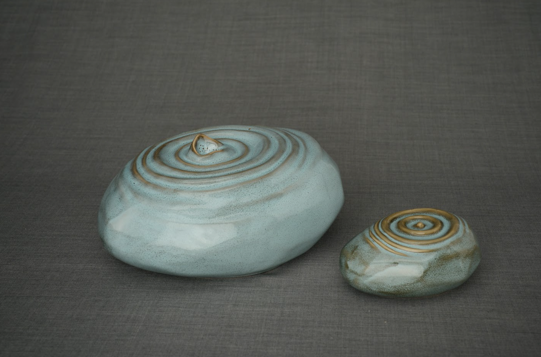 Pair of Resonance ceramic urns in seafoam blue and sage with spiral lid designs on a gray fabric backdrop