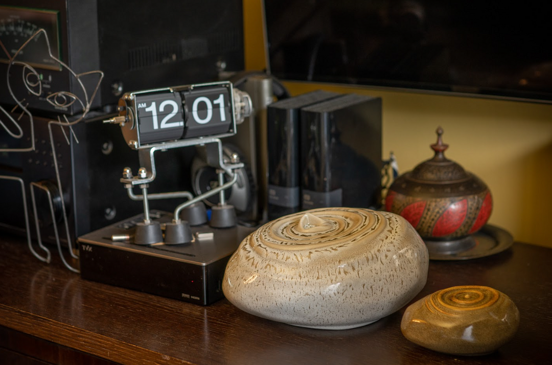 Resonance ceramic urn on a wooden desk with a vintage flip clock and decorative objects in the background.