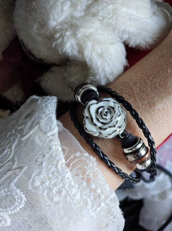 Bracelet featuring a white rose centerpiece on a pair of black braided cords with metal spacers.