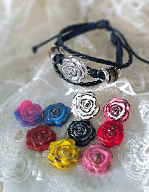 Bracelet with silver rose charm on a black braided band and colorful rose charms laid nearby.