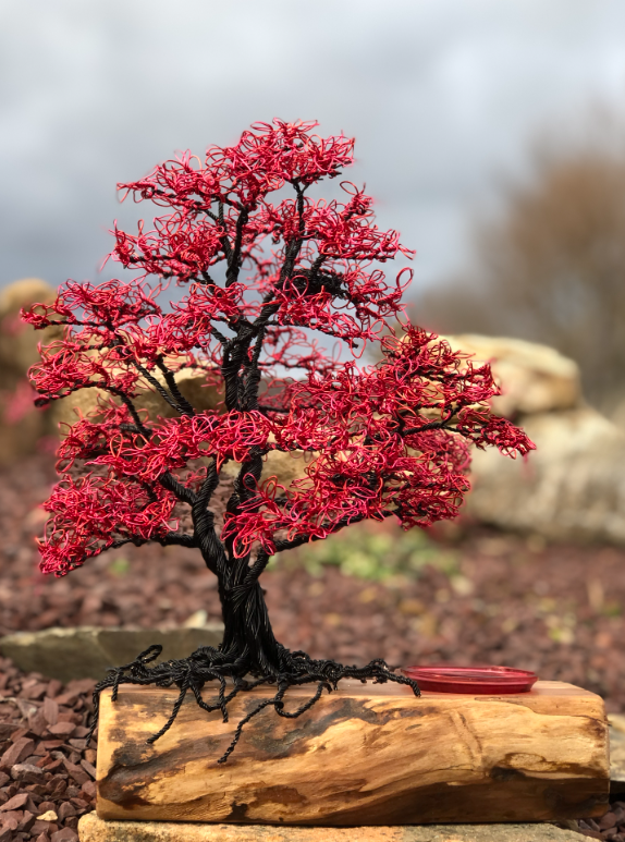 Red maple wire tree on a natural wood base with exposed roots beside a blue glass orb.