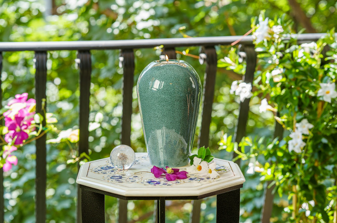 Serenity teal ceramic urn outdoors on a decorative table with flower petals and a glass decorative orb nearby