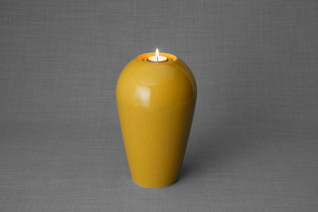 Mustard yellow ceramic urn with a lit tea light on top against a gray studio backdrop.