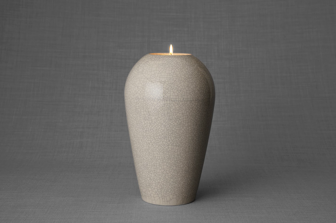 Beige crackle glaze ceramic urn with a lit tea light on top against a gray studio backdrop.