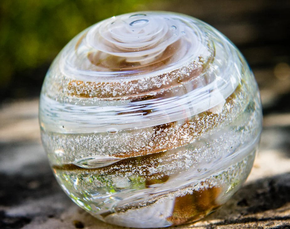 Close up of a gold amber Sparkle Orb with swirling bands on a rough outdoor surface