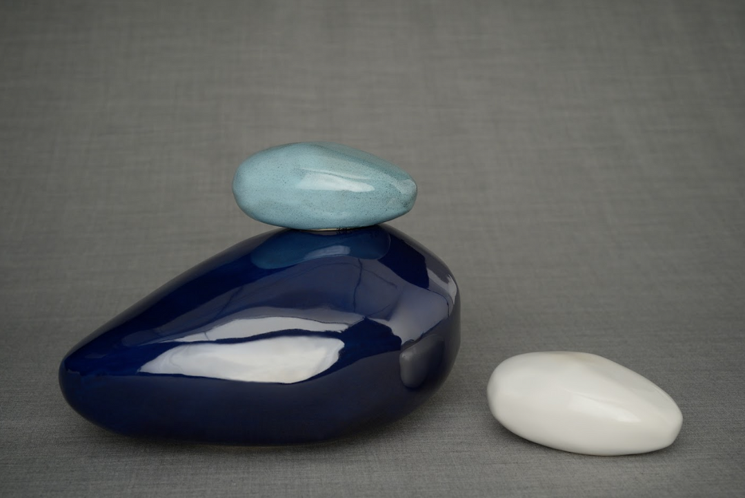 Dark blue polished stone balanced with a light blue top stone and a white pebble on a gray fabric backdrop