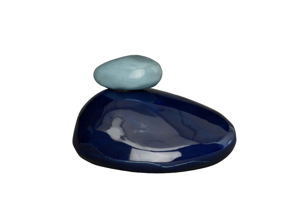 Glossy dark blue stone base with a small light blue pebble perched on top against a white background
