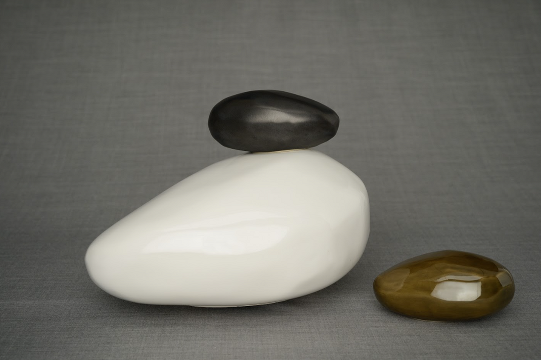 Three stones stacked with a large white base a dark top stone and a brown oval nearby on a gray backdrop