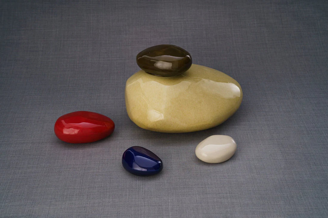 Beige stone ceramic urn with a dark lid on a smooth rounded form set against a gray background with four colored stones nearby