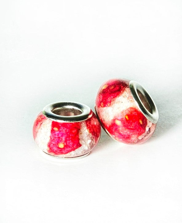 Two strawberry cheesecake cremation ash beads with red pink marbling, shown from an angled view.