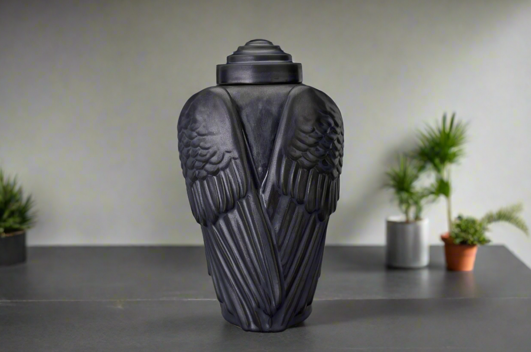 Light gray Wings Ceramic Urn with sculpted wings displayed on a desk with potted plants