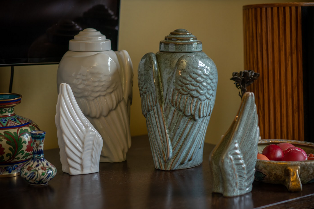White and teal Winged ceramic urns and wing sculptures arranged on a shelf with decorative items.