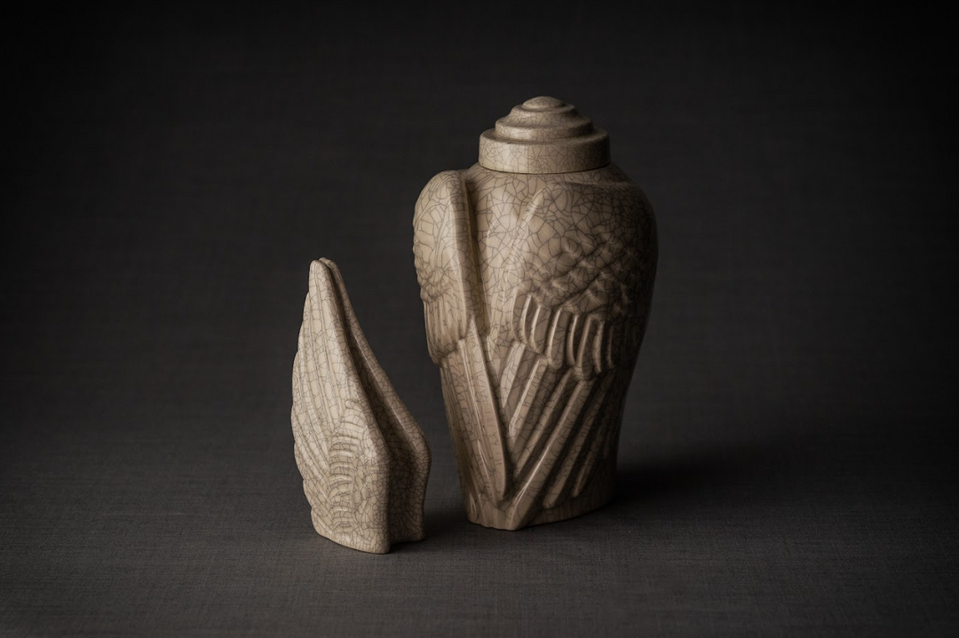 Cream Wings ceramic urn with sculpted wing motifs and a layered lid.