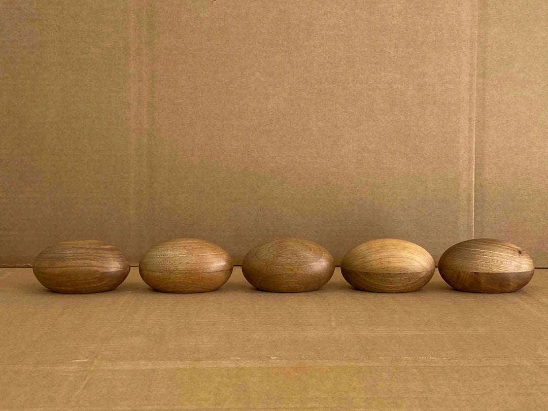 Row of five polished wooden keepsake urns in natural wood tones on a cardboard surface.