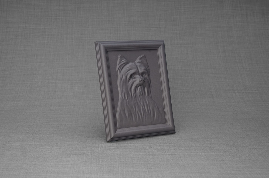 Tilted dark ceramic frame displaying Yorkie relief portrait on a gray textured backdrop.