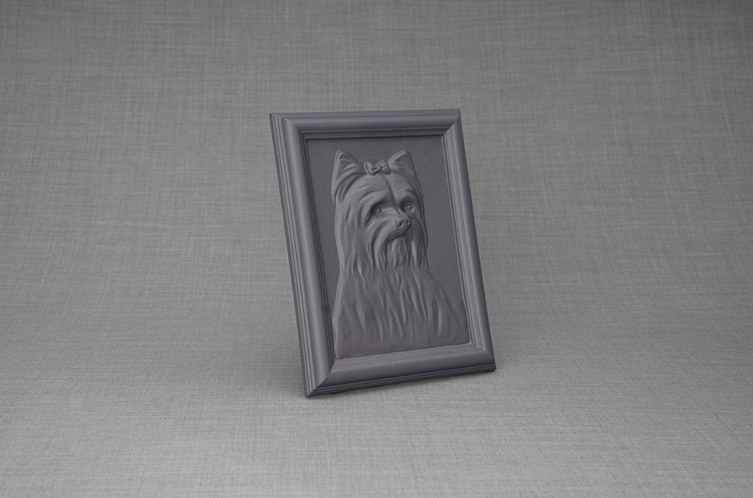 Leaning dark ceramic frame with Yorkie portrait relief set on a gray fabric background.