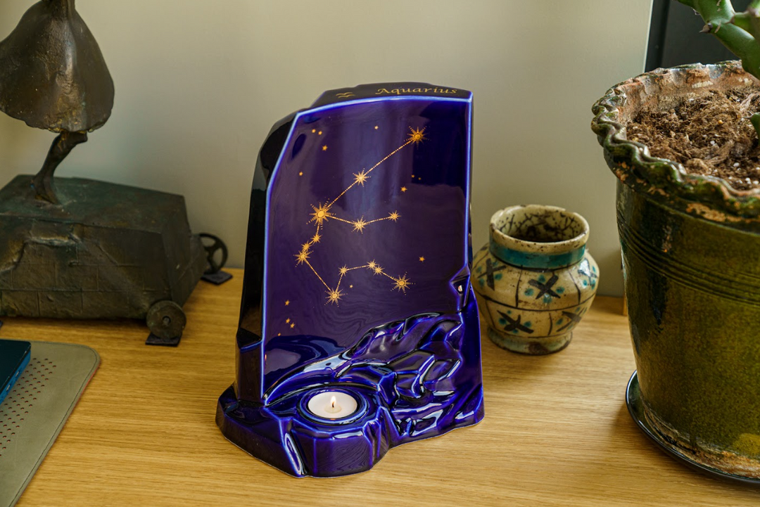 Deep blue ceramic Zodiac Urn with Aquarius constellation and a built in candle holder at the base on a wooden surface.