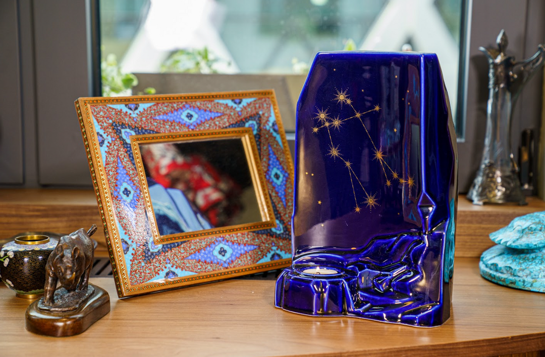 Deep blue Zodiac Ceramic Urn with a gold constellation design and a built in candle holder on a wooden display.