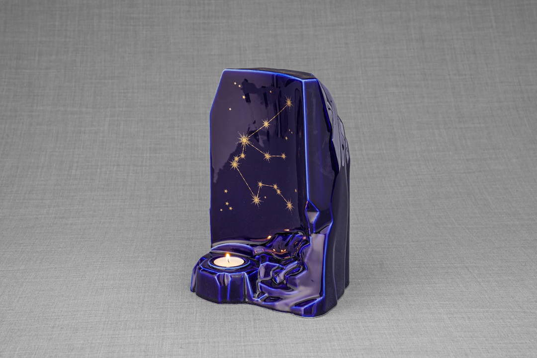 Three quarter view of deep blue Zodiac Urn showing Pisces constellation and a candle holder on a gray backdrop.