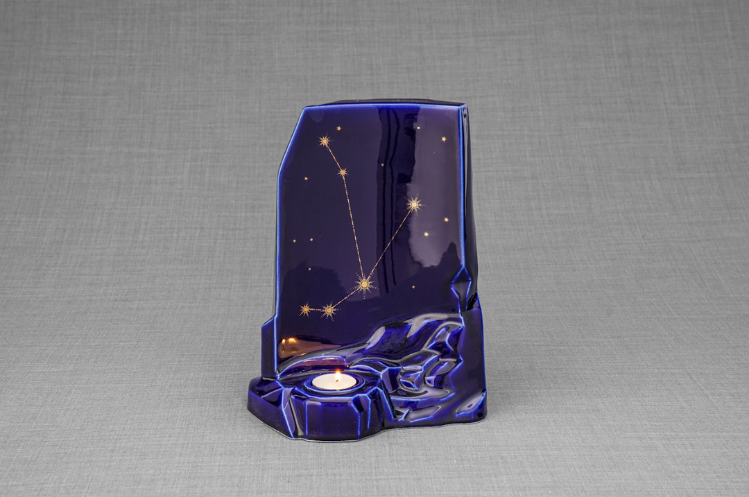 Deep blue Zodiac ceramic urn with gold constellation lines and a lit candle in the base.