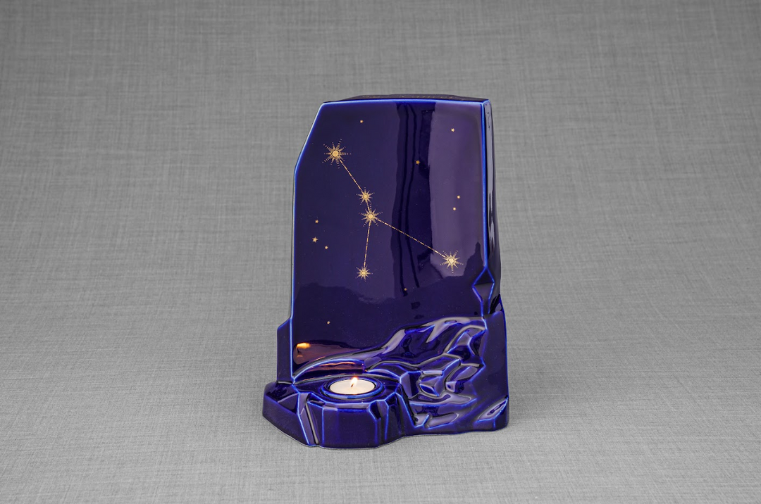 Side view of a deep blue Zodiac ceramic urn with gold constellation lines and a lit candle in the base.
