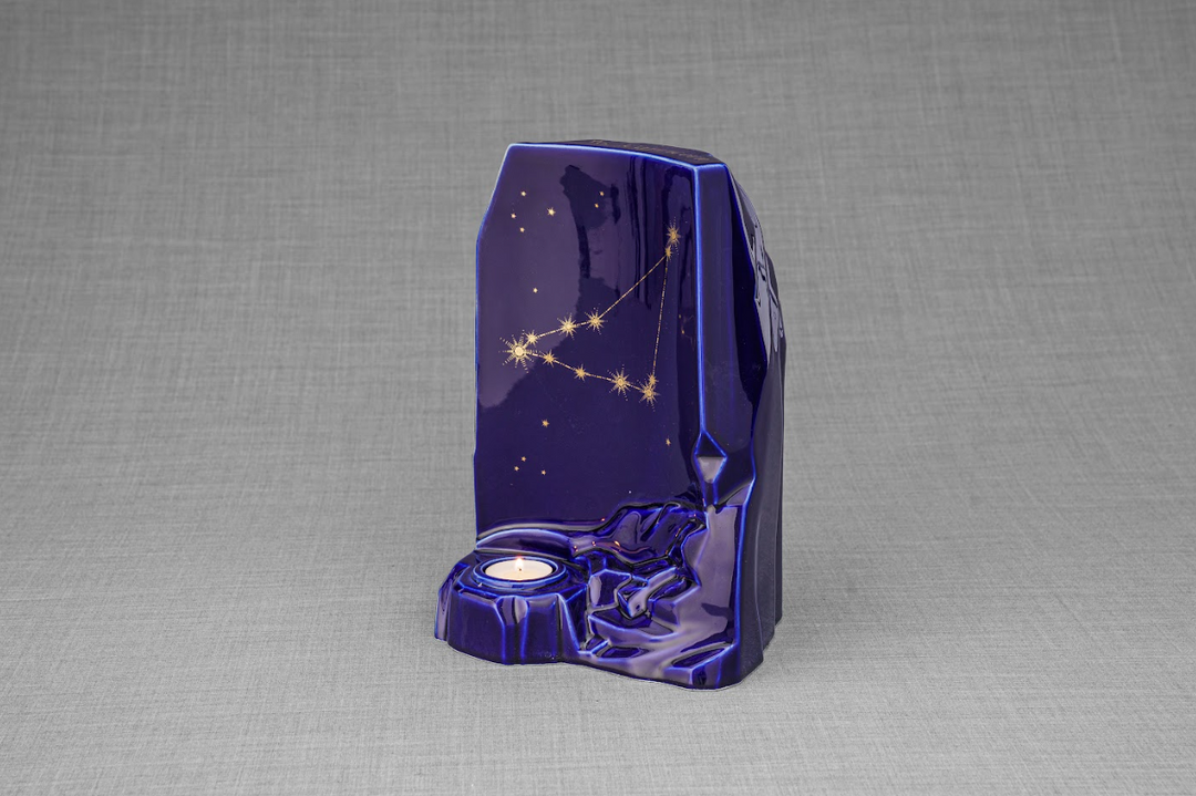 Angled view of the deep blue Zodiac ceramic urn with gold constellation pattern and a lit candle in the base.